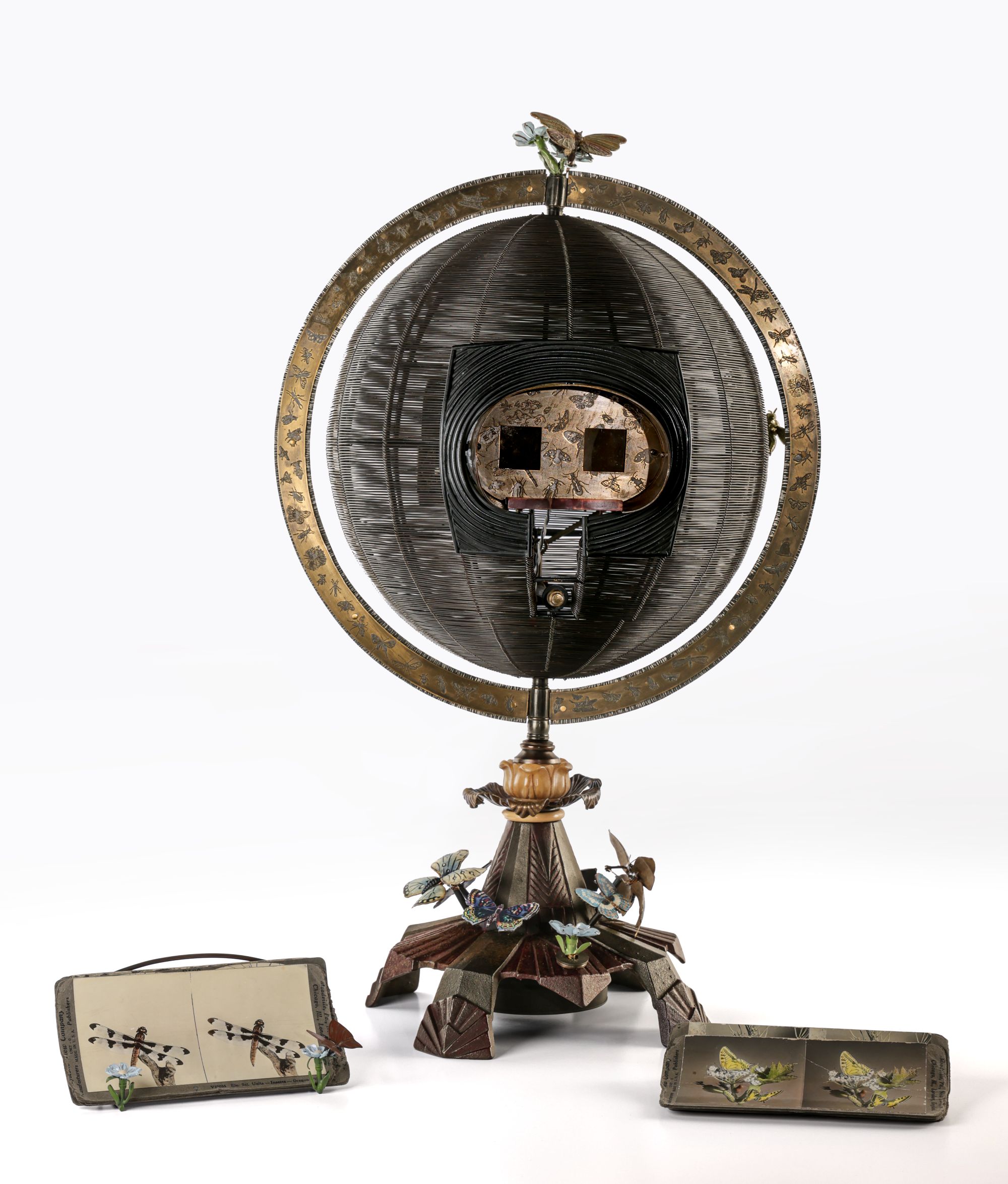 A globe-like sculpture with insects made out of steel, bronze, paint, and stereocards.